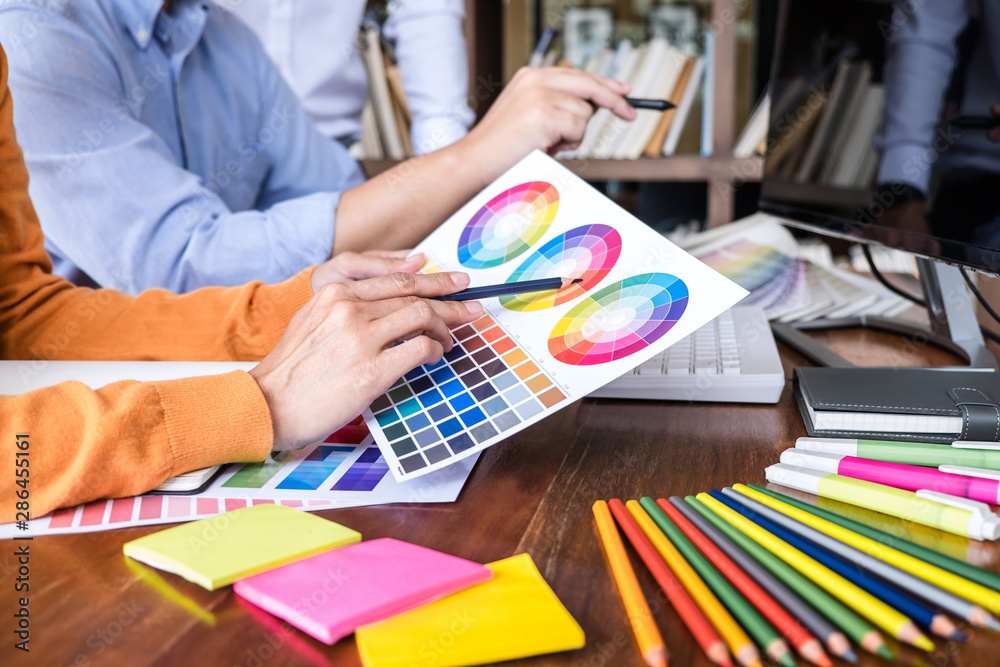 Poster Two colleague creative graphic designer working on color selection and color swatches, drawing on graphics tablet at workplace with work tools and accessories