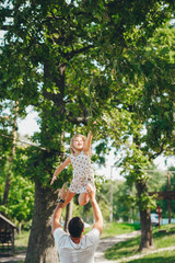 A young father throws his young daughter in the morning sunshine.