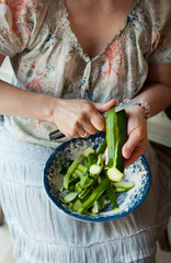 The hostess's hands peel the courgettes in a bowl.