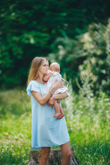 Beautiful mother in a blue dress with a child 1 year old in nature. Summer season. Motherhood.