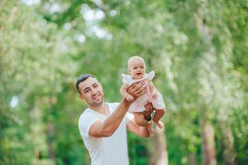 Happy father hands throws up child and looking to camera, on sunny day in the park.