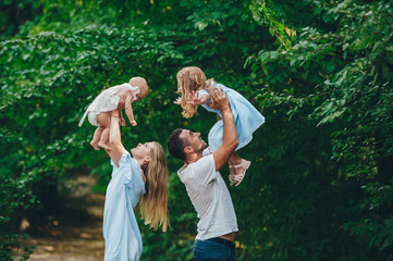 Father and mother throwing his children in the air in summer park.