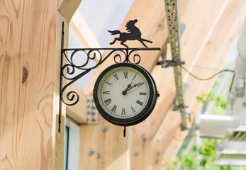 vintage black clock with porged horse on the wooden pole.