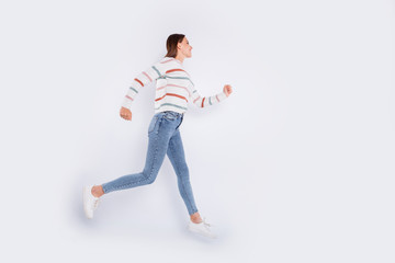 Full size profile side photo of pretty person running with beaming smile wearing striped sweater denim jeans isolated over white background