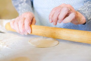 Roll the dough with a rolling pin. An old woman is cooking. For a dough dish