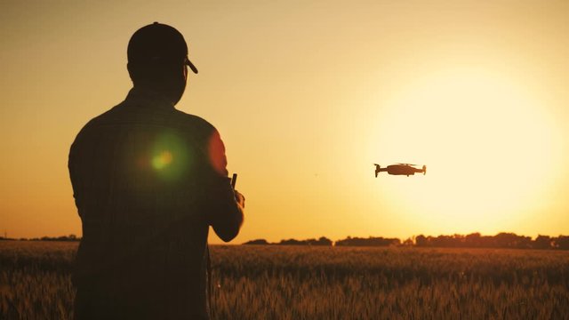 Silhouette of a farmer using a drone in a wheat field at sunset. Concept technology innovations for increasing productivity in agriculture.