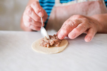 Old woman sculpts pasta. Grandma makes manti. Recipe for meat and dough.