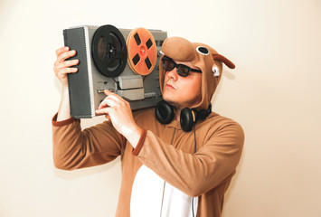 Man in cosplay costume of a cow with reel tape recorder. Guy in the animal pyjamas sleepwear. Funny photo with party ideas. Disco retro music.