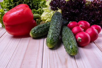 fresh vegetables on a light wooden table, paprika, celery, leaves of lettuce, cucumbers and radishes