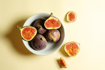 Top view fresh exotic cutted on half fig in white bowl on yellow background. Food photo background. Creative scheme of the whole and sliced figs. Flat lay. View from above. Tasty summer fruit