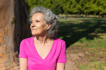 Pensive excited old waiting someone in park. Senior grey haired woman in casual sitting outdoors and looking into distance. Waiting in park concept