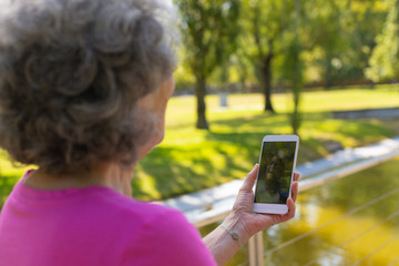Old lady talking to daughter through video call while walking in park. Senior grey haired woman in casual using mobile phone with female face on screen. Video chat concept
