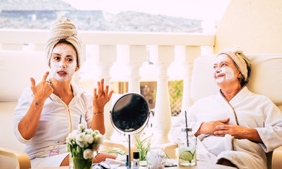Mother and daughter sitting together on the terrace taking care of their wellness. White bathrobe and towel on the hair. Peaceful and relaxing moments. Bright light