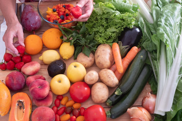 The hands of a senior woman choosing the best fruit for a fresh fruit salad. Wooden table with a large group of colorful fruits and vegetables. Healthy eating