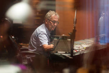 Male middle aged recording engineer in a recording studio sitting at a multi channel console