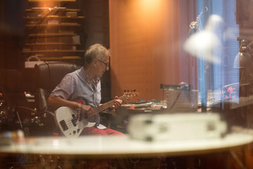 Male middle aged recording engineer in a recording studio sitting at a multi channel console - Powered by Adobe