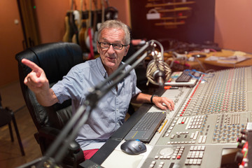 Male middle aged recording engineer in a recording studio sitting at a multi channel console