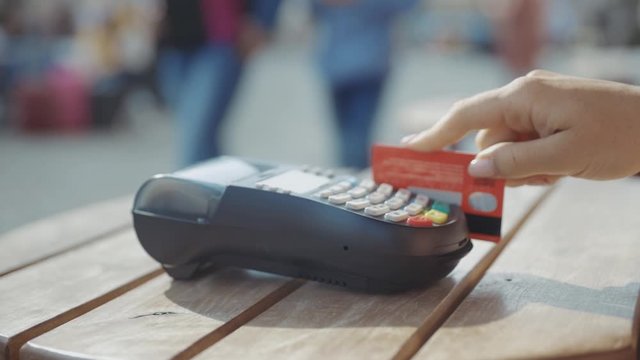 Close up hands woman paying in the cafe by credit card swiping with credit card on pos payment terminal on table in sunlight customer machine money terminal cash client electronic slow motion