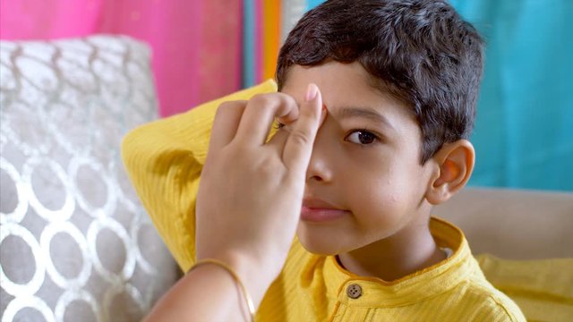 Raksha Bandhan - Little boy patiently sits while his sister applies tilak on his forehead. 