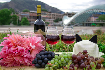 Still life on the nature of grapes, wine, hats and flowers on the background of the glass bridge of...