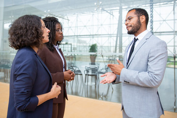 Serious businessman talking with businesswomen. Professional multiethnic male and female business colleagues standing together and talking. Teamwork concept