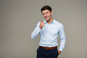 Image of cheerful brunette man wearing formal clothes smiling and pointing finger at camera while...