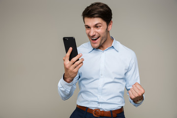 Image of ecstatic happy man wearing formal clothes smiling and looking at cellphone