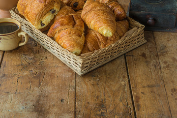 Traditional french breakfast in retro style. Basket with croissants, cup of coffee and coffee grinder on the old wooden background with copy space