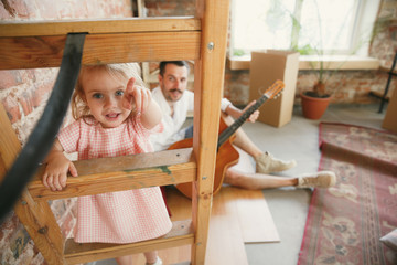 New life. Young father and his daughter moved to a new house or apartment. Look happy and confident. Moving, relations, lifestyle concept. Playing together, preparing for repair and laughting.