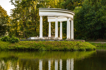 Half-rotunda with white columns near the water in a quiet park