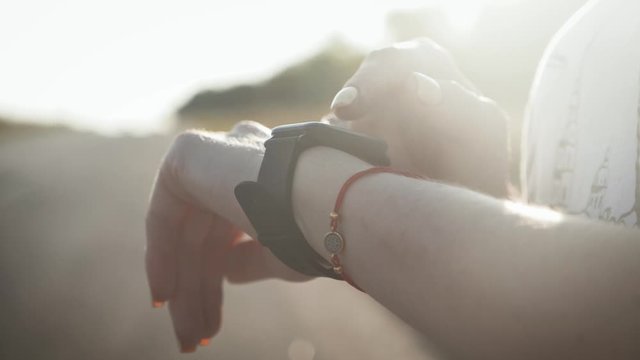 Young woman runner looking at sports smart watch, checking performance or heart rate pulse trace. Closeup of hands and wrist with smart watch screen.
