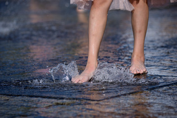 Strong heat in the city: girl&rsquo;s leg playing with fountain water jets at the square