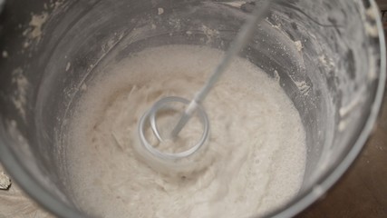 Mix the solution in a bucket using a construction mixer. Worker mixing plaster in a bucket for alignment and putty walls of the apartment using an electric drill, close-up.