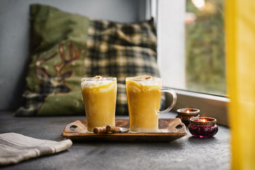 Two glass cups of pumpkin spice latte next to a window