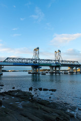 Fototapeta na wymiar Rocky waterside and Ryde Bridge with bright sky.