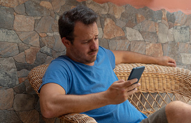Young guy looking cellphone worried reading the news and having feeling of doubt and confused....