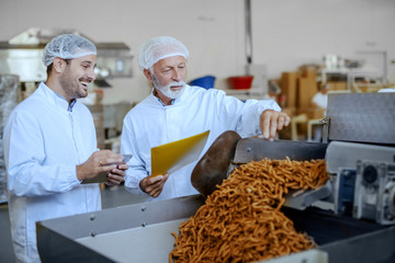 Two focused inspectors in white uniforms and hairnets evaluating quality of food. Both are dressed in white uniforms and having hairnets. Food plant interior.