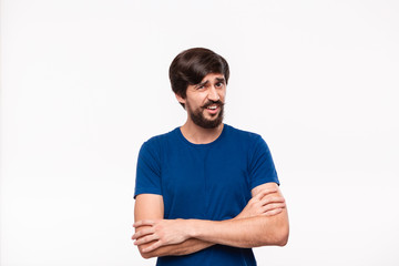 Good looking brunet man in a blue shirt holding arms folded over his chest with sceptical emotion standing isolated over white background.