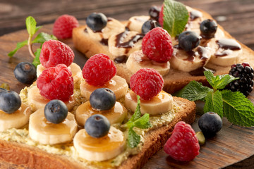 Sandwiches with banana, raspberry blueberry, blackberry and blueberry on bread with honey and chocolate and mint on a wooden table