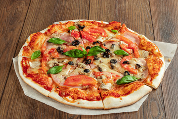 Pizza on a wooden background with ham, olives, tomatoes and green basil. Itolyan cuisine, copy space.