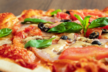 Pizza on a wooden background with ham, olives, tomatoes and green basil. Itolyan cuisine, copy space.