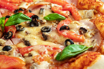 Pizza on a wooden background with ham, olives, tomatoes and green basil. Itolyan cuisine, copy space.