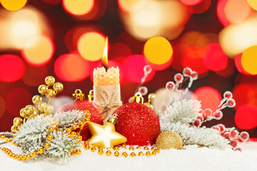 Bright Christmas composition with abstract bokeh light background, green fir branch, gold garland, red baubles, holly berries and candle on white snow background