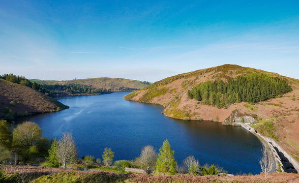 Llyn Clywedog reservoir in Wales with blue skies and trees.
