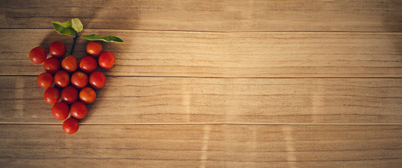 Group of sherry tomatoes forming a heart (or grape) shape on a wooden background. Selective focus. Banner, cover