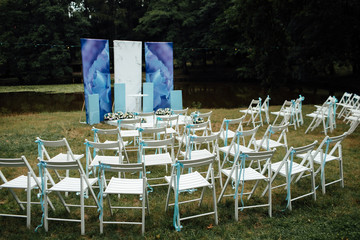 Beautiful outgoing wedding set up. Romantic wedding ceremony , wedding outdoor. Wedding decor. White wooden chairs on a green lawn. White armchairs for guests for the ceremony. 