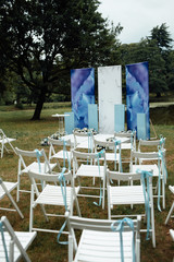 Beautiful outgoing wedding set up. Romantic wedding ceremony , wedding outdoor. Wedding decor. White wooden chairs on a green lawn. White armchairs for guests for the ceremony. 