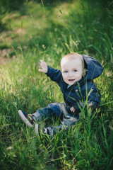 Little cute fashionable happy baby boy sitting on grass
