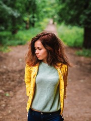 A girl with long hair and a bright yellow jacket is walking along a path in a green gloomy forest