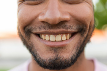 Obraz premium Closeup of smiling male face. Young Latin man with black stubble giving toothy smile. Dental care concept